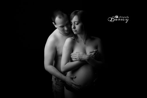 Czarno-białe zdjęcie ciężarnej pary czule obejmującej się podczas ciążowej sesji zdjęciowej.